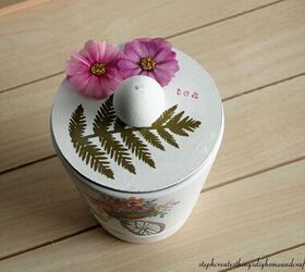 cmo hacer un encantador portabolsas de t, Maceta blanca decorada con una servilleta decorativa flores y hojas de papel y una tapa redonda de madera con una cuenta de madera