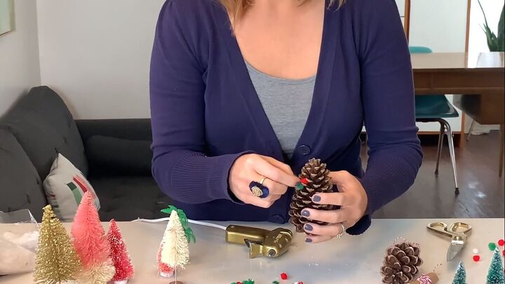 Hot-gluing pom poms to a pine cone