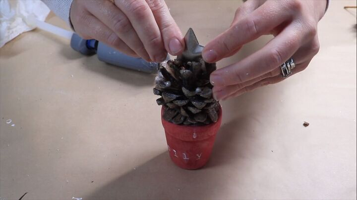 Gluing a metal star to the top of the pine cone Christmas tree