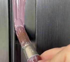 el color de puerta de entrada que nunca supe que siempre quise para mi casa gris, Primer plano de una mano utilizando una brocha para pintar de morado una puerta de entrada negra