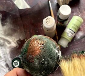 adornos vintage diy una sencilla gua de manualidades navideas, Una persona est pintando una bola verde con pintura y pinceles