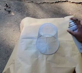 A wire trash basket being spray painted silver