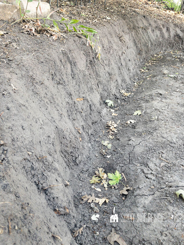 A trench is dug into the dirt for the first row of rocks for building a retaining wall