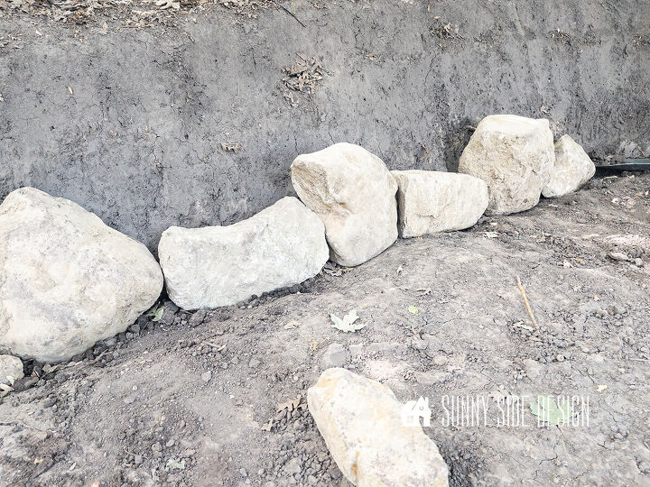 First row of rocks are placed in a trench for the retaining wall