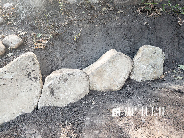 First row of rocks are placed in a trench for the retaining wall