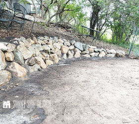 The completed stone retaining wall on a slope in a wooded backyard