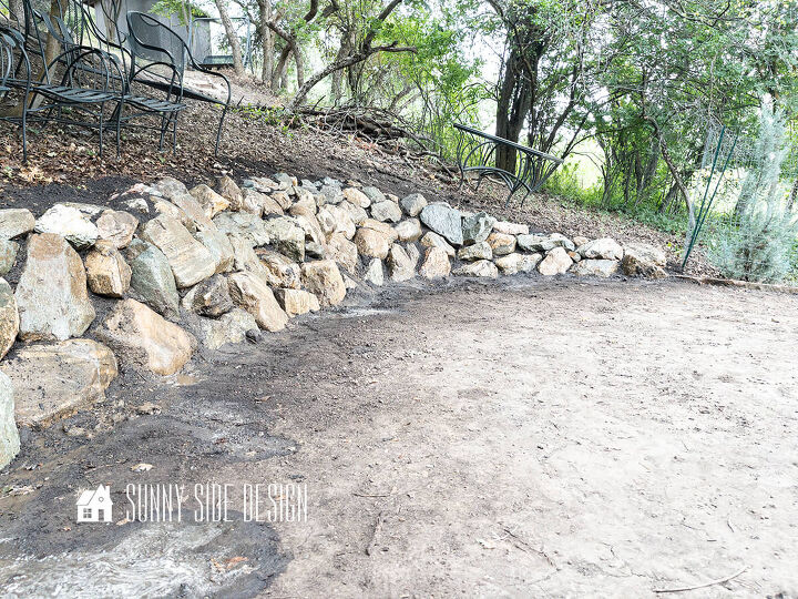 The completed stone retaining wall on a slope in a wooded backyard