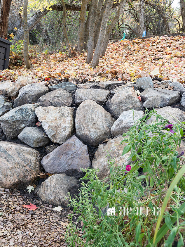 Completed rock retaining wall with autumn leaves and a green plant