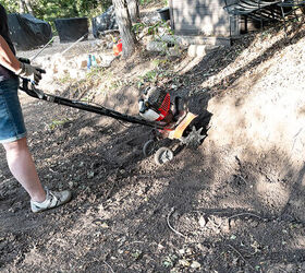Woman uses a small garden tiller to loosen the hard clay soil to prepare the area for building a stone retaining wall