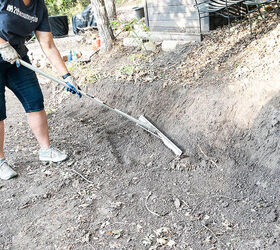 Woman uses a landscaping rake to pull the loosened soil to prepare the area for a stone retaining wall