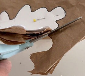 With a oak leaf template pinned to recycled brown paper a woman cuts out the shape of an oak leaf