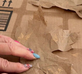 A woman rubs gold Rub n Buff on a brown packing paper maple leaf