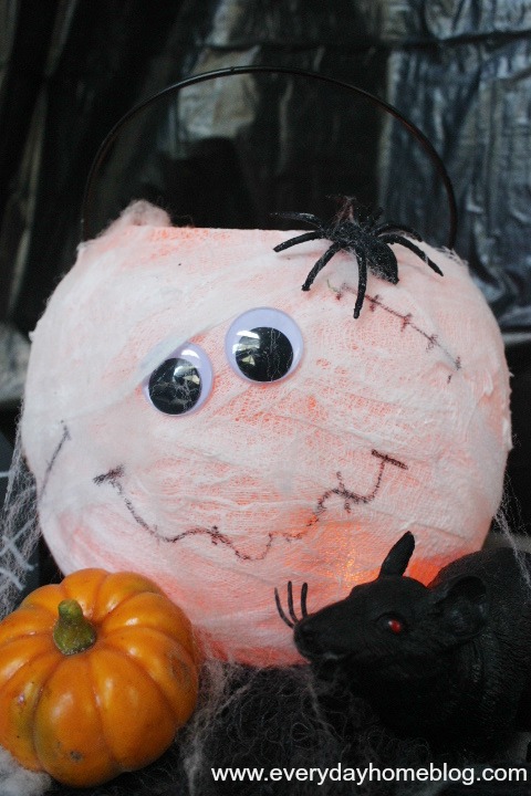 mason jar mummy lanterns, crafts, halloween decorations, mason jars, seasonal holiday decor, Meet the Mum pkin Its a Dollar Store plastic pumpkin pail wrapped in cheese cloth with googley eyes and a drawn on smile and scars So easy