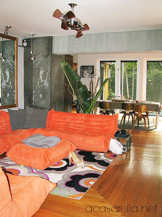 tropical industrial home tour, home decor, outdoor living, pool designs, Funky orange couches add a pop of contrast against the concrete walls
