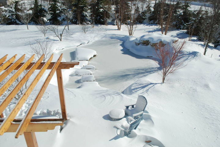i think this pond is more beautiful in the snow what do you think, outdoor living, ponds water features, spas, View from the frozen pond from the bedroom deck The deck and Bullfrog Spa are covered by snow You can see the boulder stepping stones and Moss Rock Island in the middle of the pond