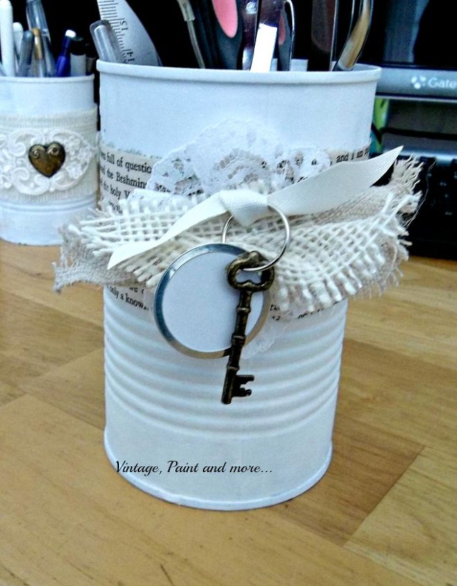 recycled and decorated tin cans, crafts, repurposing upcycling, After painting them I decorated them by gluing on all sorts of bits and pieces This one has a bit of book page wrapped around it then a small medallion of lace with burlap and ribbon added Lastly a key and label