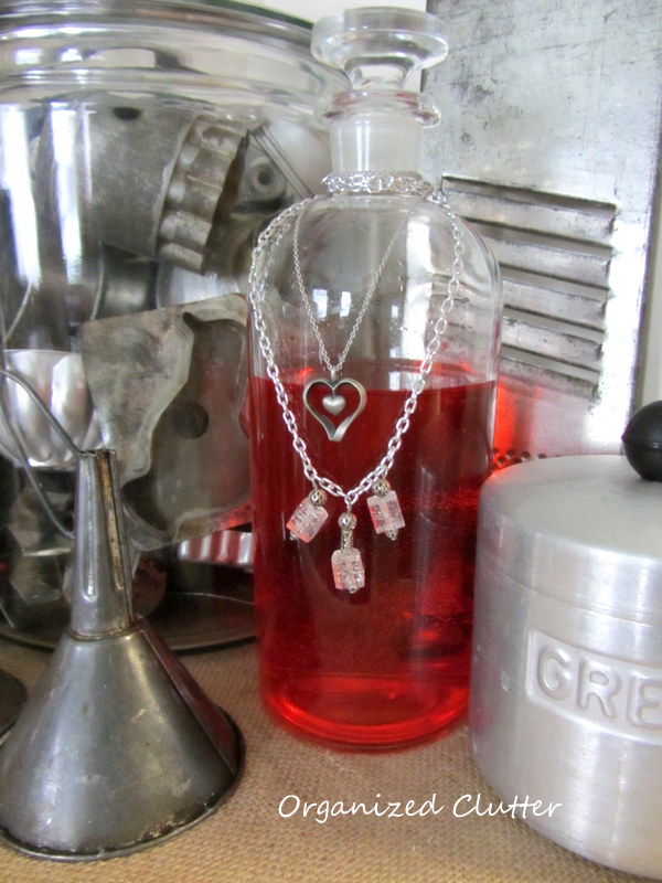 thrift shop heart valentine s day craft, christmas decorations, repurposing upcycling, seasonal holiday d cor, valentines day ideas, Clear glass bottles with red food coloring are great Valentine s Day decor especially when adorned with thrift shop necklaces