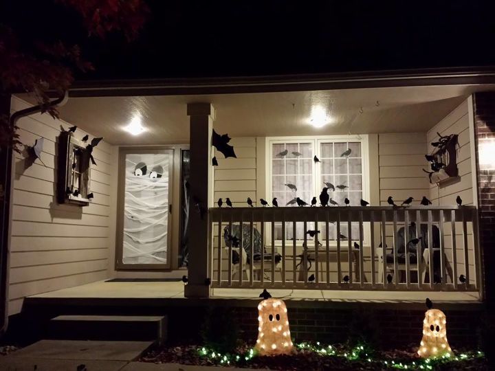 front porch halloween decorating idea, halloween decorations, seasonal holiday d cor, This is my sister s creative Halloween decorating idea Sandra turned her porch into spooky land rather cleverly Cute lighted pumpkins welcome trick or treaters but once they pass cute they enter darkness Black birds Too many black birds black like the night Flying around and sitting on her porch railing chilling the spine A ghost guards the door