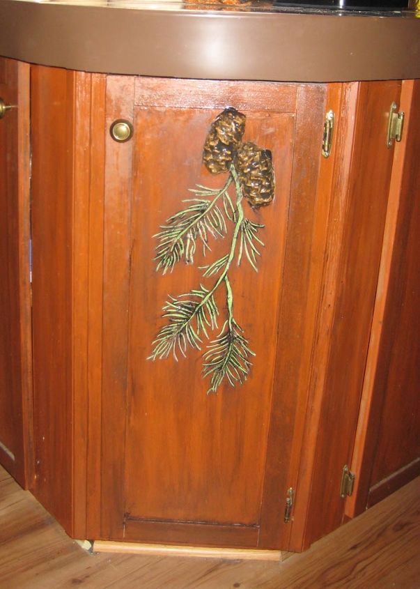 rustic kitchen cabinets get a country design with plaster stencils, home decor, kitchen cabinets, kitchen design, The pine cones were cast from a mold primed and painted then attached over the pine branch design A coat of varnish protects the design