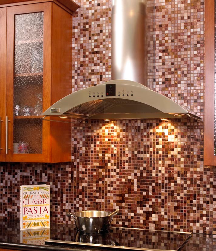 The backsplash for the range was created with thousands of multi-colored unique glass tiles in various blended shades to create this beautiful feature wall. Numbered for placement, these tiles -- with hand applied 24-karat gold leaf between two layers of glass -- give a dark-to-light effect. The backsplash goes up the wall and highlights the sleek, European-style, stainless steel range hood with four halogen lamps that extends down from the ceiling, while also complementing the cabinetry on both sides.