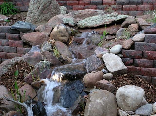 water features through walls, gardening, landscape, outdoor living, ponds water features, wall decor, Located off the owner s deck this waterfall cascades down a very steep hill through the retaining wall and flows into a large pond filled with beautiful koi at Arvada CO